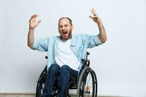 une homme dans une fauteuil roulant regards à le caméra colère et agression, avec tatouages sur le sien bras est assis sur une gris studio arrière-plan, santé concept homme avec handicapées photo