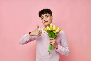 portrait de une Jeune homme dans une rose chemise avec une bouquet de fleurs faire des gestes avec le sien mains modèle studio photo