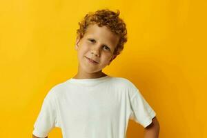 garçon avec frisé cheveux dans une blanc T-shirt sur une Jaune Contexte photo