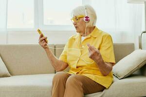 content personnes âgées femme à la recherche dans sa téléphone vidéo appel avec écouteurs sourire, La technologie pour communication, brillant moderne intérieur, mode de vie en ligne la communication photo