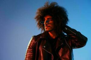 portrait de une élégant homme avec frisé cheveux sur une bleu Contexte multinational, coloré lumière, branché lunettes, moderne concept. photo