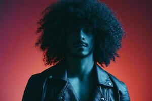 portrait de mode homme avec frisé cheveux sur rouge Contexte multinational, coloré lumière, noir cuir veste s'orienter, moderne concept. photo