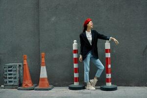 mode femme permanent penché contre une mur rue contre une Contexte de le ville route travaux touristique dans élégant vêtements avec rouge lèvres et rouge béret, voyage, cinématique couleur, rétro ancien style. photo