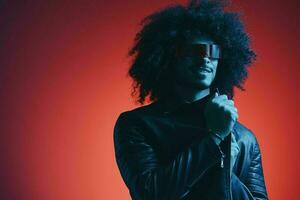 portrait de mode homme avec frisé cheveux sur rouge Contexte avec élégant lunettes, multiculturel, coloré lumière, noir cuir veste s'orienter, moderne concept. photo