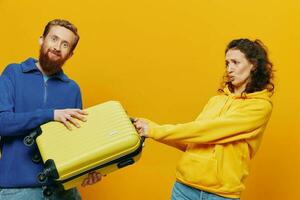 femme et homme souriant, les valises dans main avec Jaune et rouge valise souriant joyeusement et courbé, Jaune arrière-plan, Aller sur une voyage, famille vacances voyage, jeunes mariés. photo