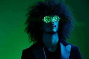 mode portrait de une homme avec frisé cheveux sur une vert Contexte avec des lunettes de soleil, multinational, coloré rose lumière, branché, moderne concept. photo