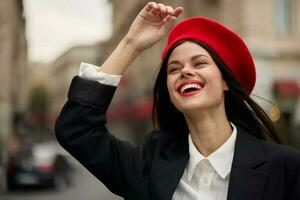 mode femme portrait sourire avec les dents permanent sur le rue dans de face de le ville touristique dans élégant vêtements avec rouge lèvres et rouge béret, voyage, cinématique couleur, rétro ancien style, Urbain mode. photo