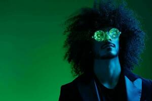 mode portrait de une homme avec frisé cheveux sur une vert Contexte avec des lunettes de soleil, multinational, coloré rose lumière, branché, moderne concept. photo