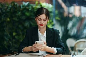 une femme blogueur touristique est assis dans une café à une table avec une téléphone dans sa mains, mobile la communication et le l'Internet dans printemps voyage, vidéo affaires appel, free-lance travail en ligne, sourire avec les dents photo