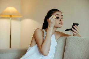 une femme à Accueil regards dans le miroir et appliquer maquillage colorant mascara cils, beauté concept, se soucier pour problème peau avec acné. photo