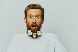 portrait de une marrant homme dans une blanc T-shirt avec fleurs marguerites dans le sien barbe sur une blanc isolé arrière-plan, copie lieu. vacances concept et toutes nos félicitations. photo