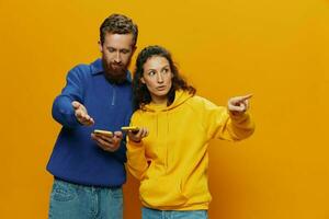 femme homme de bonne humeur couple avec Téléphone (s dans main social la mise en réseau et la communication courbé sourire amusement et lutte, dans Jaune Contexte. le concept de réel famille des relations, indépendants, travail en ligne. photo