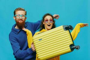 femme et homme sourire séance sur valise avec Jaune valise sourire, sur bleu arrière-plan, emballage pour voyage, famille vacances voyage. photo