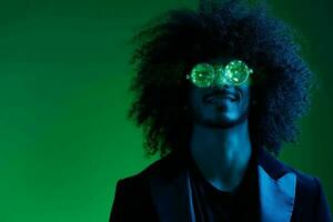 mode portrait de une homme avec frisé cheveux sur une vert Contexte avec des lunettes de soleil, multinational, coloré rose lumière, branché, moderne concept. photo