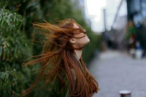 portrait de une magnifique Jeune fille dans le ville avec une magnifique sourire et rouge cheveux dans une vert imperméable dans le ville contre une Contexte de bambou dans printemps, mode de vie dans le ville photo