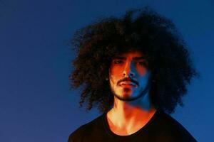 portrait de une élégant homme avec frisé cheveux dans fumée sur une bleu Contexte multinational, Couleur lumière, branché, moderne concept. photo