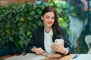 mode femme blogueur touristique est assis dans une café avec une téléphone dans sa mains lit une message, mobile la communication et le l'Internet dans Voyage printemps, vidéo appel, free-lance travail en ligne, sourire photo