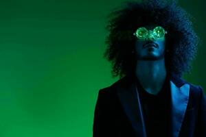 mode portrait de une homme avec frisé cheveux sur une vert Contexte avec des lunettes de soleil, multinational, coloré rose lumière, branché, moderne concept. photo