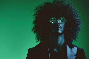 mode portrait de une homme avec frisé cheveux sur une vert Contexte avec des lunettes de soleil, multinational, coloré rose lumière, branché, moderne concept. photo