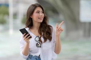Portrait de jeune femme avec visage souriant à l'aide d'un téléphone se promène dans une ville photo