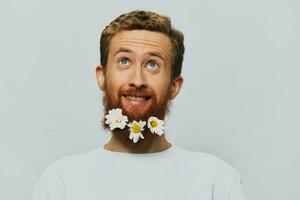 portrait de une marrant homme dans une blanc T-shirt avec fleurs marguerites dans le sien barbe sur une blanc isolé arrière-plan, copie lieu. vacances concept et toutes nos félicitations. photo