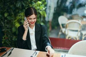 une femme blogueur touristique est assis dans une café à une table avec une téléphone dans sa mains parlant sur le téléphone, mobile les communications et le l'Internet sur une printemps voyage, affaires appel, free-lance travail en ligne, sourire photo