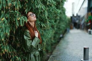 portrait de une mode femme avec rouge en volant cheveux avec des lunettes sur une Contexte de vert des arbres bambou dans le ville sourire avec dents, le concept de mode et style dans le ville photo