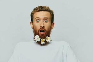 portrait de une marrant homme dans une blanc T-shirt avec fleurs marguerites dans le sien barbe sur une blanc isolé arrière-plan, copie lieu. vacances concept et toutes nos félicitations. photo