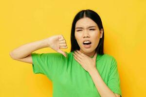 portrait asiatique magnifique Jeune femme dans vert t-shirts gestes avec le sien mains émotions Jaune Contexte inchangé photo