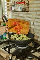 chef ajoute haché tomates à le pot avec le Ingrédients sur le gaz le fourneau photo