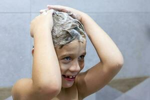 enfant d'âge préscolaire garçon lavages le sien tête avec le sien mains dans le salle de bains avec shampooing photo