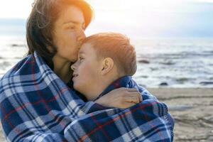 mère et sa fils sont relaxant sur le plage enveloppé dans une plaid plaid photo