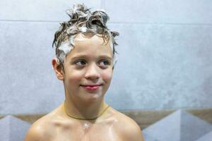 garçon lavages le sien tête dans le salle de bains avec shampooing photo