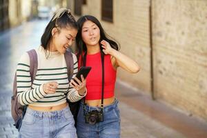 asiatique les filles touristes en marchant sur ville rue avec téléphone intelligent photo