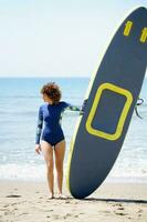 méconnaissable surfeur avec planche à pagaie sur sablonneux plage photo
