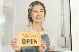 propriétaire affaires détail, attrayant asiatique Jeune femme main dans tournant signe planche à ouvert café boutique, rouvrir boutique après proche verrouillage quarantaine dans COVID-19 [feminine. photo
