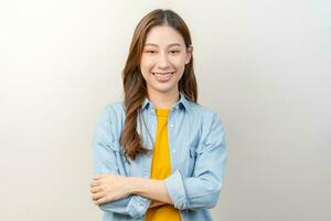 sourire positif, attrayant asiatique Jeune femme portant occasionnel, portrait de magnifique brunette sa avec longue cheveux, sentiment content à la recherche à caméra, permanent traverser bras poitrine isolé sur blanc Contexte. photo