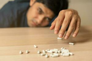 proche en haut drogue bouteille, verser nombreuses pilules sur tableau. stressé, asiatique Jeune homme, Masculin prendre médecine, mensonge sur table à maison, abuser de surdosage et toxicomane. malade douleur de santé traitement, suicide déprimé. photo