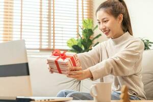 célébrer sur Noël veille, Nouveau année journée saison, jolie asiatique Jeune femme, fille en utilisant portable ordinateur, salutation sur vidéo appel pendant social distance, en portant cadeau boîte, content à avoir cadeau, joyeux Noël photo