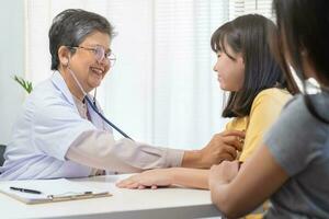 mature asiatique médecin psychiatre, général femme médecin consultant concerné avec adolescent fille, enfant patient, en utilisant stéthoscope à écouter, rendez-vous à clinique. santé se soucier, vérifier en haut médical. photo