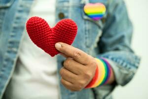 une dame asiatique portant des bracelets de drapeau arc-en-ciel et tenant un coeur rouge, symbole du mois de la fierté lgbt célèbre chaque année en juin les droits des gays, lesbiennes, bisexuels, transgenres et humains. photo