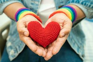 une dame asiatique portant des bracelets de drapeau arc-en-ciel et tenant un coeur rouge, symbole du mois de la fierté lgbt célèbre chaque année en juin les droits des gays, lesbiennes, bisexuels, transgenres et humains. photo