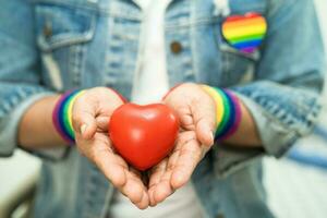 une dame asiatique portant des bracelets de drapeau arc-en-ciel et tenant un coeur rouge, symbole du mois de la fierté lgbt célèbre chaque année en juin les droits des gays, lesbiennes, bisexuels, transgenres et humains. photo