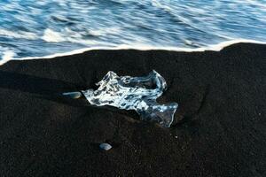 vague s'écraser iceberg fusion sur noir le sable plage dans le le coucher du soleil à diamant plage photo