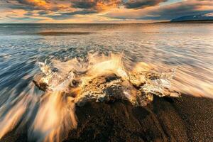 vague s'écraser iceberg fusion sur noir le sable plage dans le le coucher du soleil à diamant plage photo