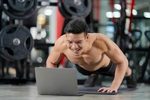 Formation en ligne sport homme formation faisant des push ups exercice avec ordinateur portable dans la salle de fitness