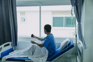 asiatique Masculin patient mensonge sur lit avec visage masque dans récupération pièce dans hôpital salle. tout gens portant masque à prévenir covid19 virus infection pendant coronavirus pandémie. le homme se sent solitaire et trou. photo