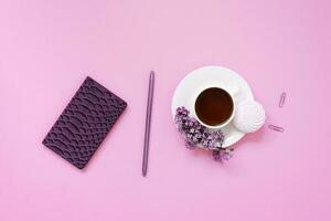 une tasse de thé, des cahiers, un stylo, un bouquet de lilas sur fond violet. fleurs printanières violettes. pause thé au travail blogueur ou employé de bureau photo