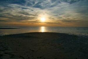 coucher de soleil, vue plus de le sablonneux plage à le illuminé mer. lumière vagues. baltique mer photo