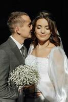 une élégant jeune marié tendrement baisers le de la mariée joue. magnifique la mariée avec moderne bouquet embrassement élégant jeune marié dans magnifique lumière. sensuel romantique moment. mariage. élégant et magnifique photo